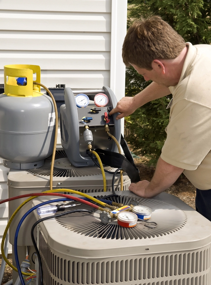 Technician performing maintenance on an outdoor AC condenser with pressure gauges.