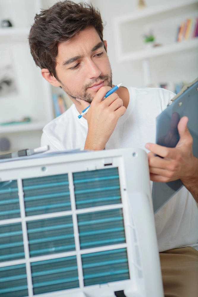 Man inspecting HVAC filter system and reviewing notes for troubleshooting.