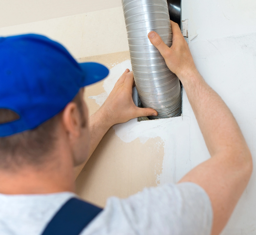 Worker installing or inspecting flexible ductwork into a wall vent.